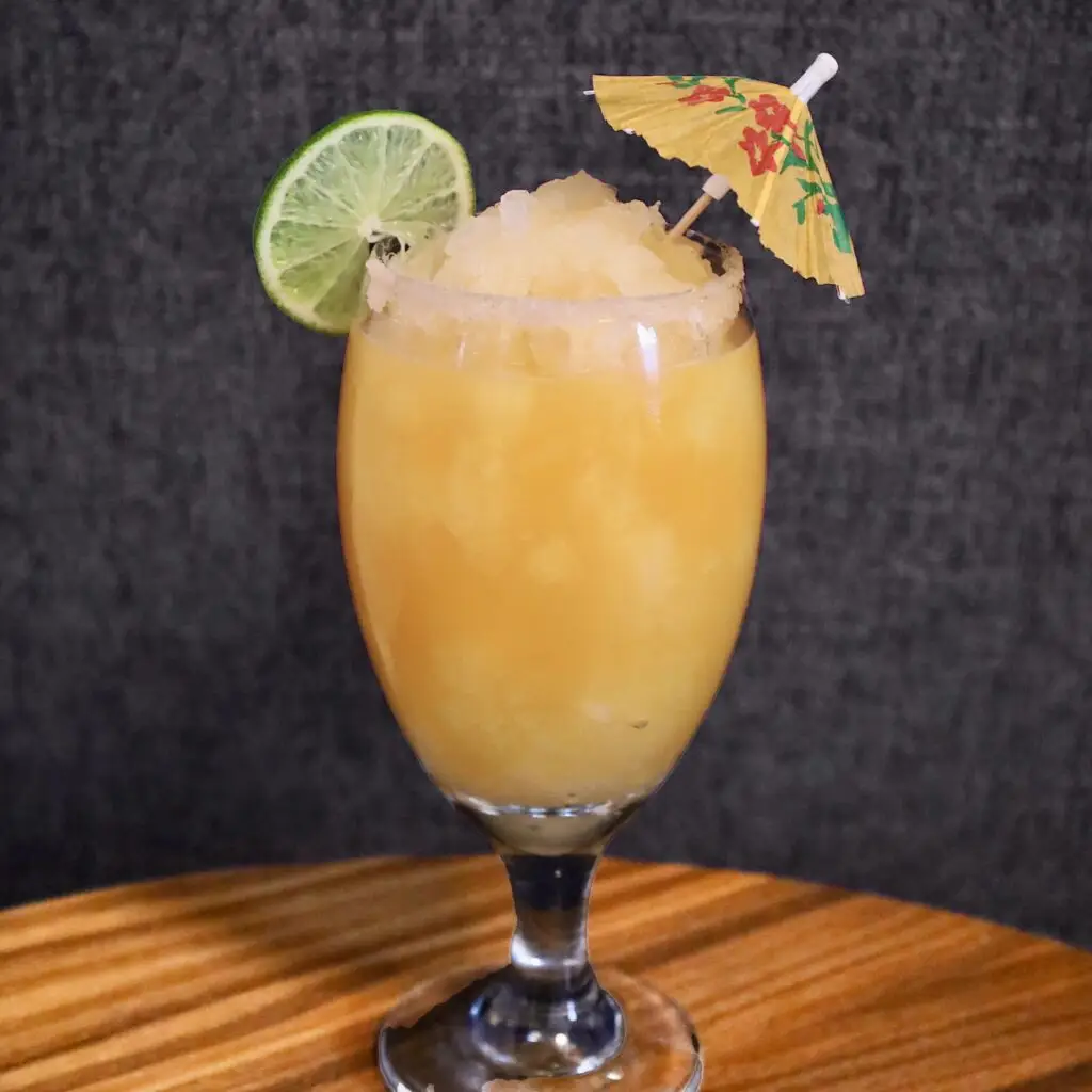 Drinks XXL Mango Daiquiri served in a glass with lime slice and cocktail umbrella garnish.