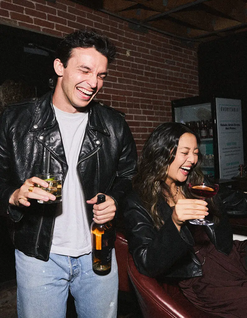 Two friends enjoying Drinks XXL flavored wines, laughing together in a lively, casual setting.